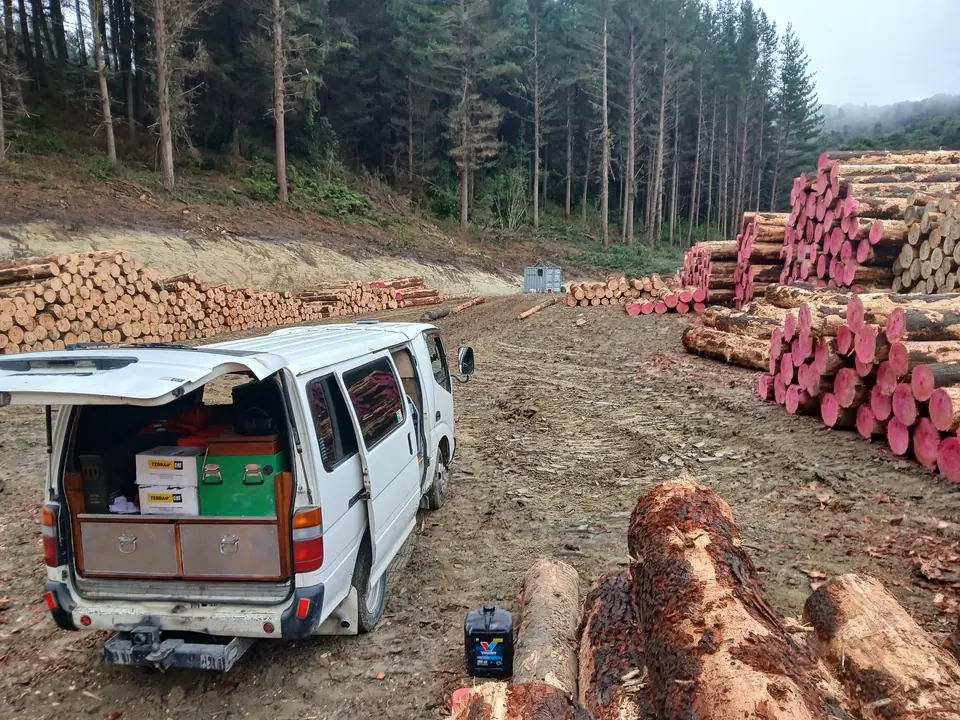 Service van opened up with tools and gear out beside stacked logs