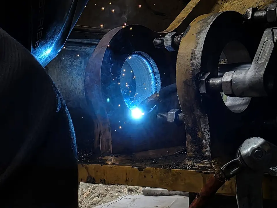Welding arc lighting up the gap between two boom lugs during a repair